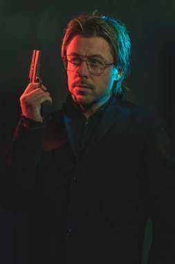 Man holding gun next to his head. Illminated by red and blue lig