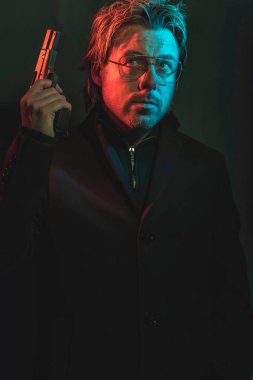 Man holding gun next to his head. Illminated by red and blue lig