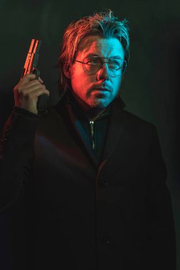 Man holding gun next to his head. Illminated by red and blue lig
