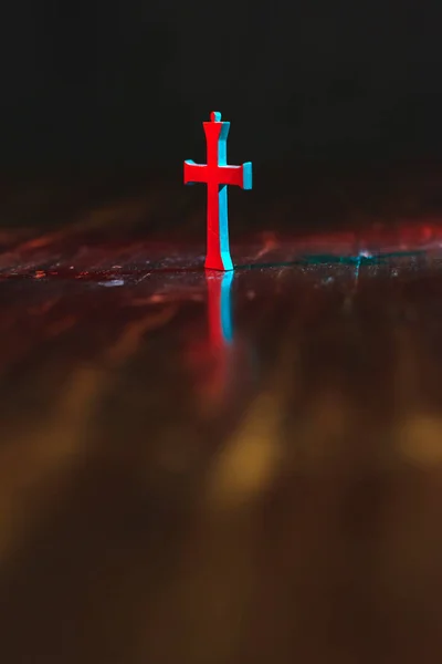 Vecchio piccolo crocifisso su tavolo di legno in luce rossa e blu a nig — Foto Stock