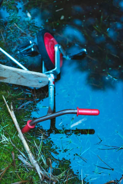 Övergivna barn trehjuling i pöl av mörkt vatten i skogen. — Stockfoto