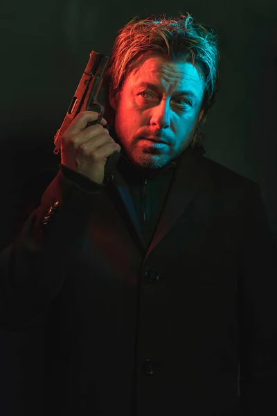 Egy férfi pisztolyt tart a feje mellett. Vörössel és kékkel megvilágítva — Stock Fotó