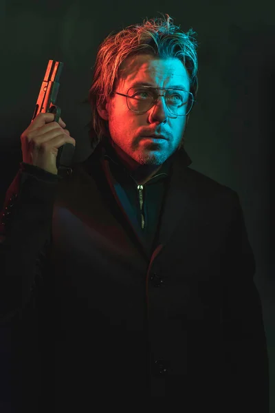Un hombre sosteniendo un arma junto a su cabeza. Ilustrado por la tapa roja y azul —  Fotos de Stock