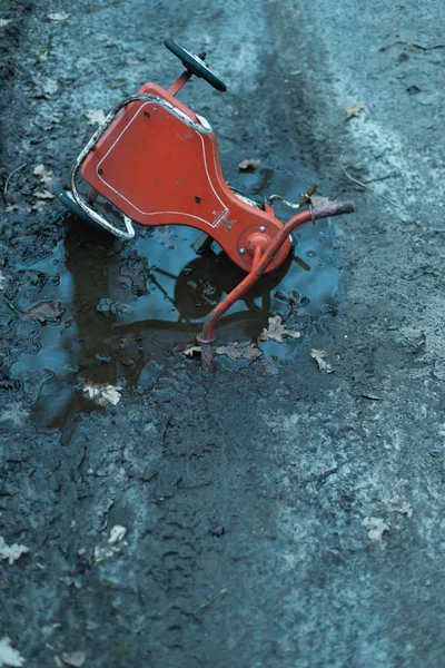 Triciclo abandonado caído em poça na estrada de terra na floresta . — Fotografia de Stock