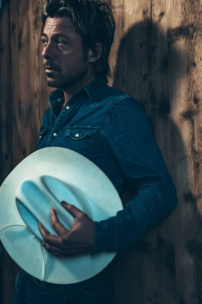 Man Denim Shirt Holding Cowboy Hat Standing Wooden Wall — Stock Photo, Image