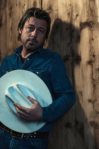 Mannen Jeansskjorta Håller Cowboyhatt Stående Vid Trävägg — Stockfoto
