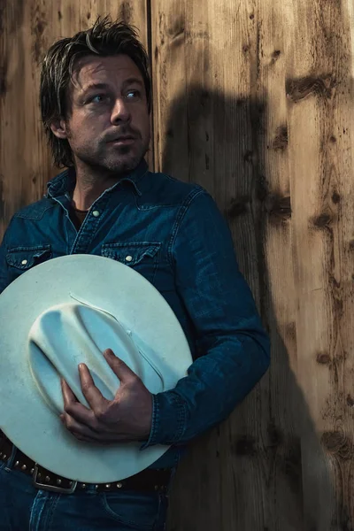 Man Denim Shirt Holding Cowboy Hat Standing Wooden Wall — Stock Photo, Image