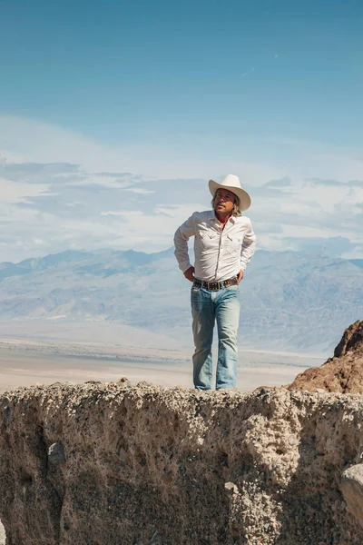 砂漠の風景の中の岩の上に白いカウボーイハットの男 — ストック写真