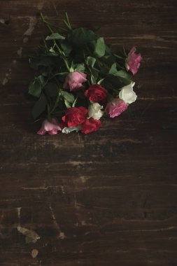 Ahşap masada bırakılmış kırmızı, pembe ve beyaz güller..