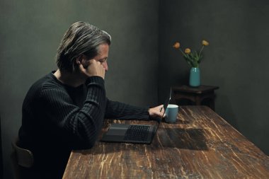 Evde çalışan dizüstü bilgisayarın arkasındaki adam. Yan görünüm.