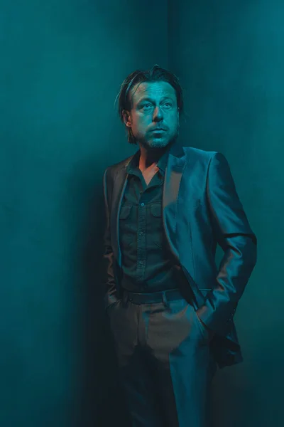 Man in suit stands in corner of empty room. Serious and pensive expression.