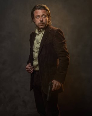 Gri duvarın önünde koyu kahverengi takım elbiseli, orta yaşlı, şık bir adam. Alçak sesli stüdyo çekimi.