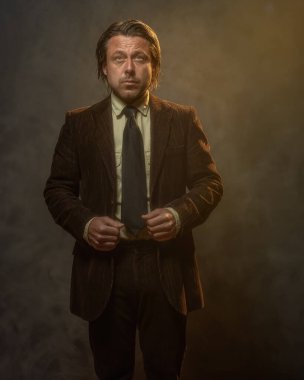 Koyu kahverengi takım elbiseli ve gri duvarın önünde siyah kravatlı havalı orta yaşlı iş adamı. Alçak sesli stüdyo çekimi.