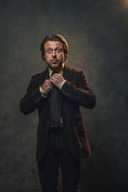 Koyu kahverengi takım elbiseli ve gri duvarın önünde siyah kravatlı havalı orta yaşlı iş adamı. Alçak sesli stüdyo çekimi.