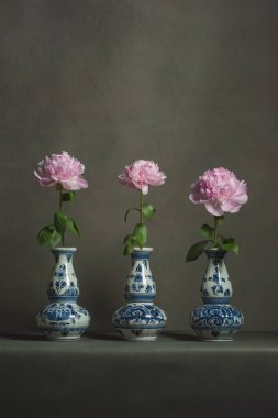 Gri bir odadaki masada pembe şakayıklı üç delft mavi vazo..