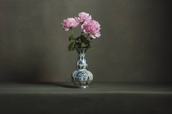 Pink peonies in a delft blue vase on a table in a grey room.