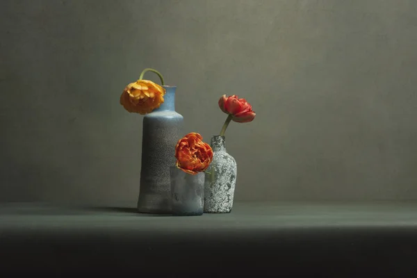 Three vintage vases with red and orange peony tulips in grey room.