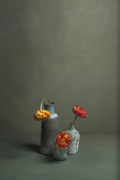 Three vintage vases with red and orange peony tulips in grey room.