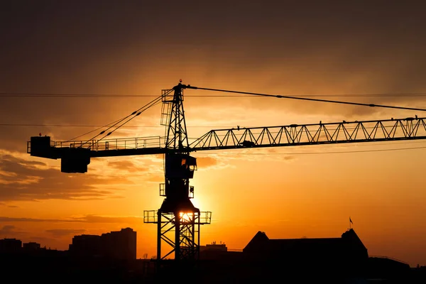 Industrial construction crane silhouette over sun at sunrise.