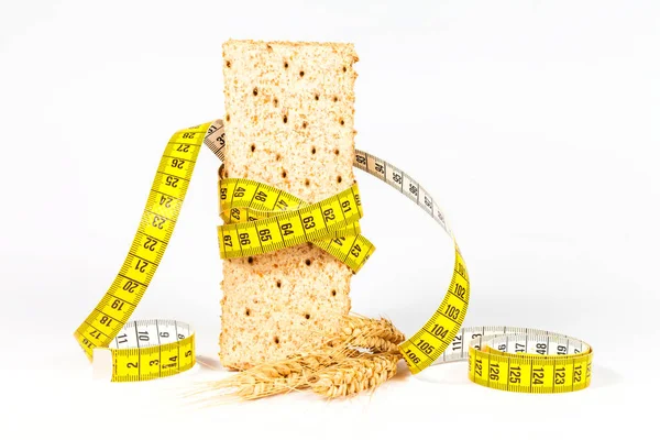 Ein gelbes Maßband, das Weizencracker oder Knäckebrot und Weizengarbe umwickelt - gesundes Ernährungskonzept — Stockfoto