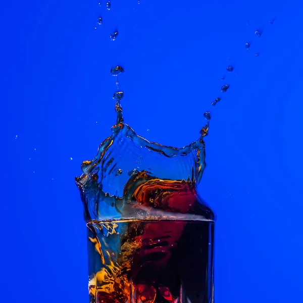 Vidrio con salpicadura de whisky sobre fondo azul —  Fotos de Stock