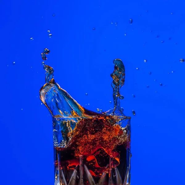 Vidrio con salpicadura de whisky sobre fondo azul — Foto de Stock