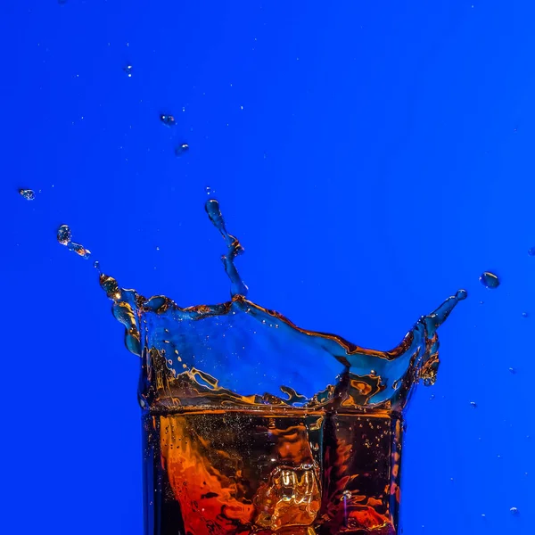 青の背景にウイスキー スプラッシュとガラス — ストック写真