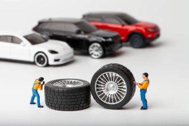 Atölye lastiği provası konsepti. Minyatür tamirciler oyuncak araba tekerleğini tamir ediyor. Kapatın..