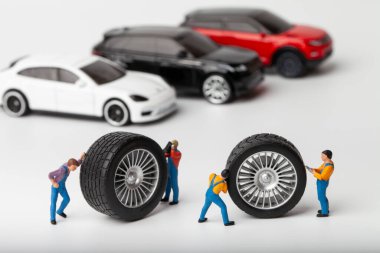 Atölye lastiği provası konsepti. Minyatür tamirciler oyuncak araba tekerleğini tamir ediyor. Kapatın..