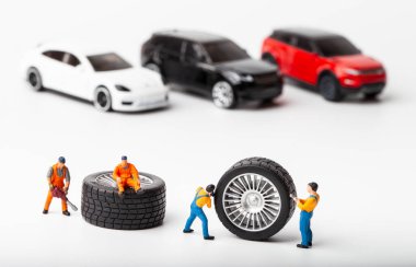Atölye lastiği provası konsepti. Minyatür tamirciler oyuncak araba tekerleğini tamir ediyor. Kapatın..