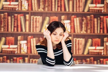 bir kitaplıktaki kitapların bir arka plan üzerine bir masada oturan güzel kız öğrenci