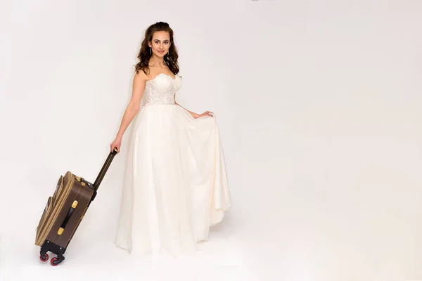 美丽的新娘在白色婚纱礼服不同的姿势白色背景与旅行袋 — 图库照片