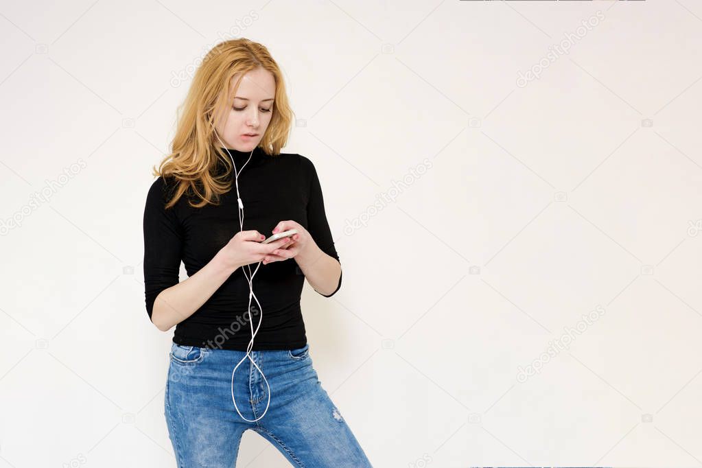 Portrait of a beautiful blonde girl on a white background looking carefully and pushing on a smartphone.