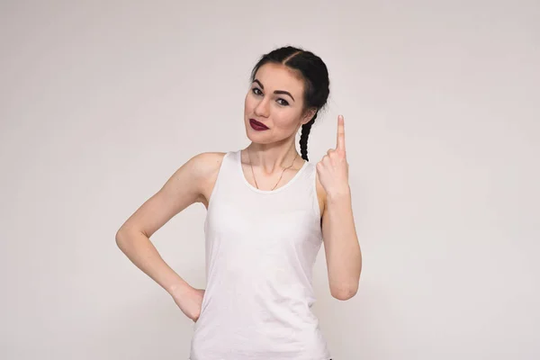 Portrait of a beautiful brunette girl in a T-shirt on a gray background showing a number one finger — Stock Photo, Image