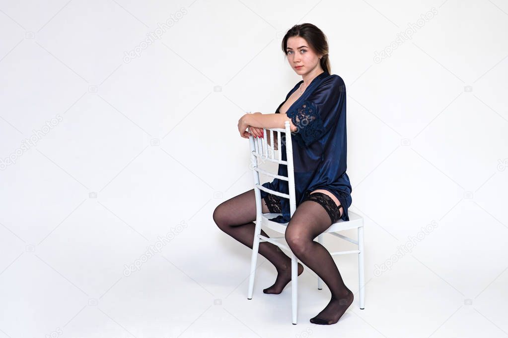 Portrait of a beautiful girl on a white background in lingerie on a chair.