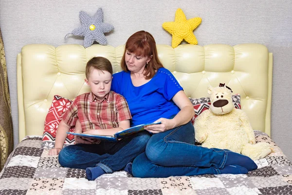 Mom and son are sitting on the bed and reading a book