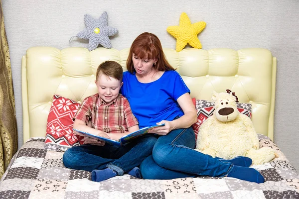 Mom and son are sitting on the bed and reading a book — Stock Photo, Image