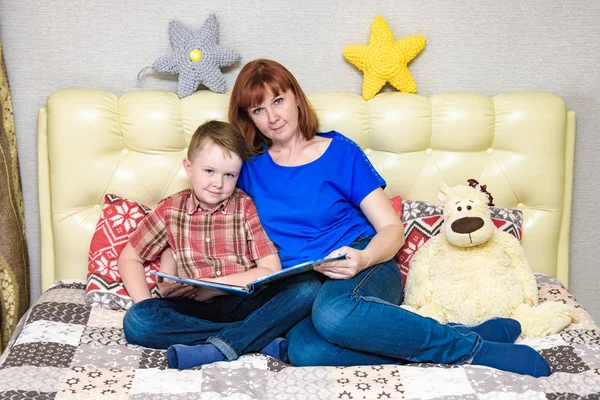 Mom and son are sitting on the bed and reading a book — Stock Photo, Image