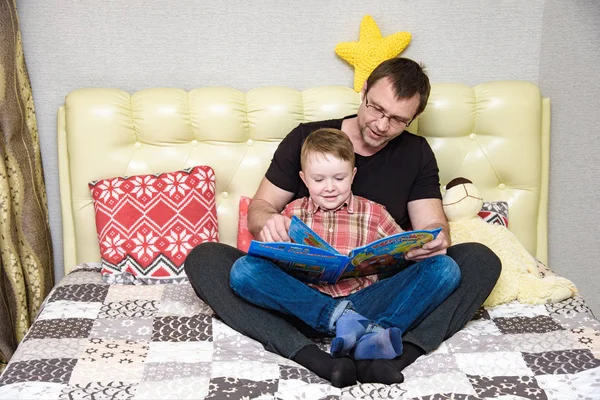 Батько і син сидять на ліжко і читати книгу. — стокове фото