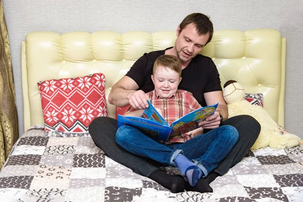 Dad and son are sitting on the bed and reading a book. — Stock Photo, Image