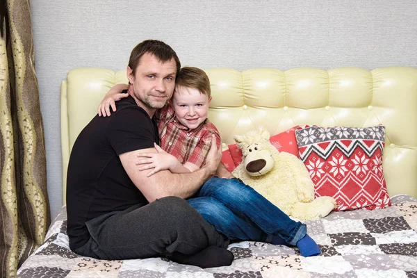 Dad and son are hugging sitting on the bed. — Stock Photo, Image