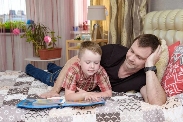 Pai e filho leram um livro deitado na cama . — Fotografia de Stock
