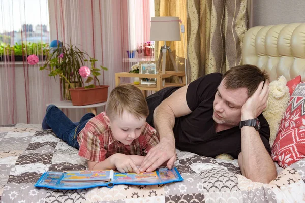 Pai e filho leram um livro deitado na cama . — Fotografia de Stock