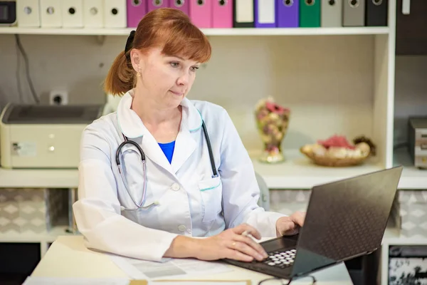 Médico sentado no escritório com laptop e trabalhando — Fotografia de Stock