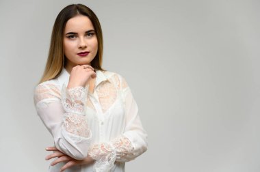 Güzel bir kızın stüdyo portresi. Uzun güzel saçları ve gri arka planda mükemmel bir makyajı var. Kameraya konuşuyor..