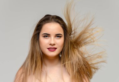 Uzun, dalgalı saçları ve gri bir arka planda farklı pozlarda mükemmel makyajı olan güzel bir kızın büyük stüdyo fotoğrafı. Gülümsüyor..