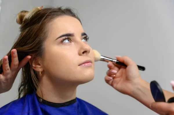 Foto de estúdio do trabalho de um maquiador por um esteticista cabeleireiro. Criando maquiagem bonita e penteados, rejuvenescendo a pele do rosto. O profissional está trabalhando com ferramentas especiais . — Fotografia de Stock