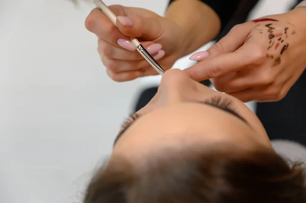 Foto de estúdio do trabalho de um maquiador por um esteticista cabeleireiro. Criando maquiagem bonita e penteados, rejuvenescendo a pele do rosto. O profissional está trabalhando com ferramentas especiais . — Fotografia de Stock