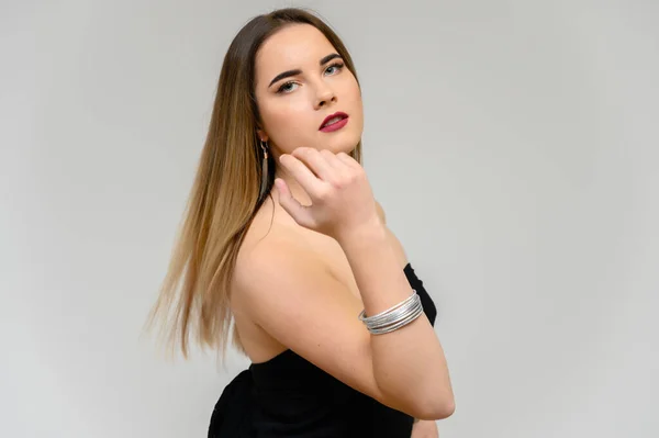 Retrato de estudio de una hermosa chica con cabello largo y hermoso y excelente maquillaje sobre un fondo gris en diferentes poses. Ella sonríe . — Foto de Stock