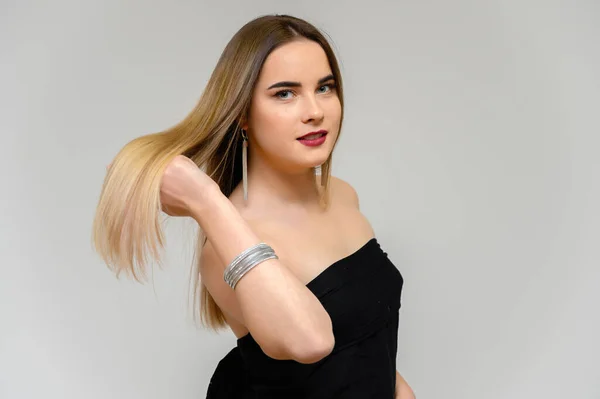 Retrato de estudio de una hermosa chica con cabello largo y hermoso y excelente maquillaje sobre un fondo gris en diferentes poses. Ella sonríe . — Foto de Stock